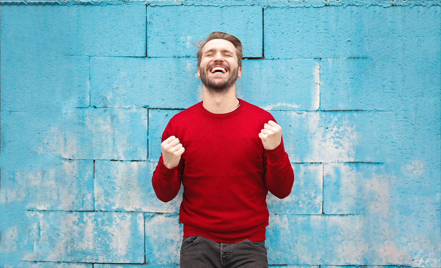 happy man rejoicing wearing red shirt standing in front of blue wall